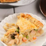 A serving of chicken pie with a golden crust and mixed vegetables on a white plate.
