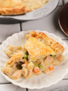 A serving of chicken pie with a golden crust and mixed vegetables on a white plate.