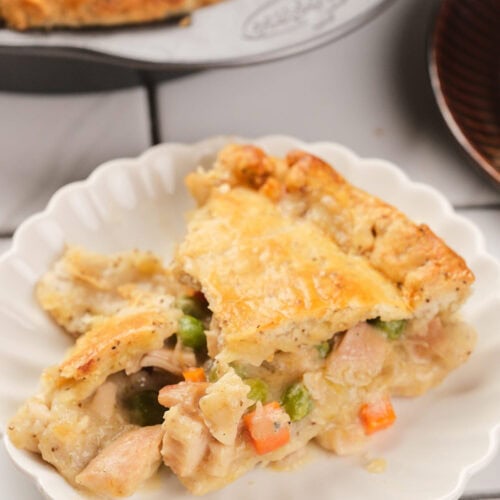 A serving of chicken pie with a golden crust and mixed vegetables on a white plate.