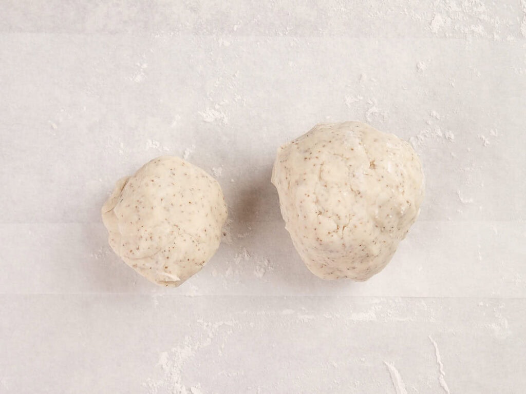 Two balls of dough of different sizes rest on a sheet of parchment paper lightly dusted with flour.