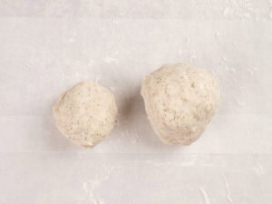 Two balls of dough of different sizes rest on a sheet of parchment paper lightly dusted with flour.