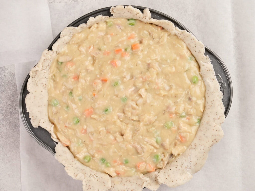 Unbaked pot pie filled with a creamy mixture of chicken, peas, carrots, and creamy sauce in a round baking pan.