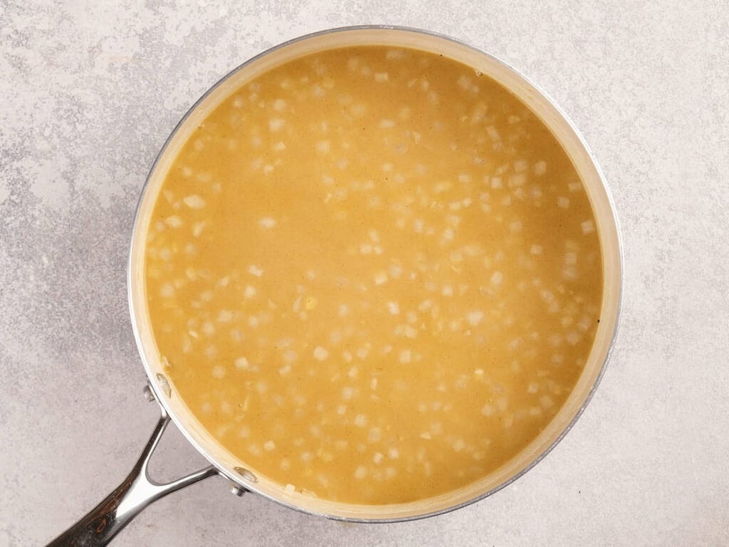 A pot of soup with onions in it on a light surface.
