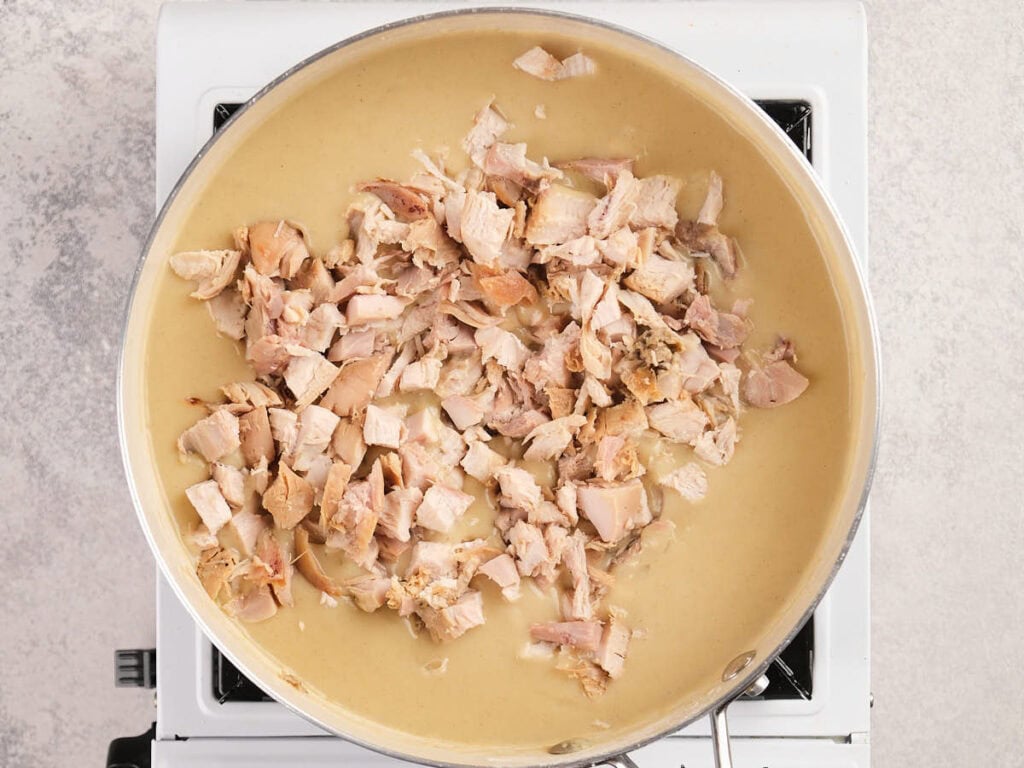 A pan of chopped cooked chicken in creamy sauce sits on a stovetop burner.