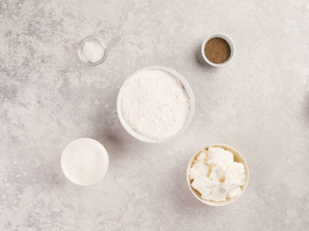 Five ingredients for a pie crust are arranged on a light textured surface.