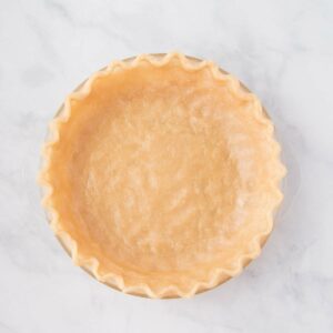 Unbaked pie crust with crimped edges in a glass pie dish on a white marble surface.
