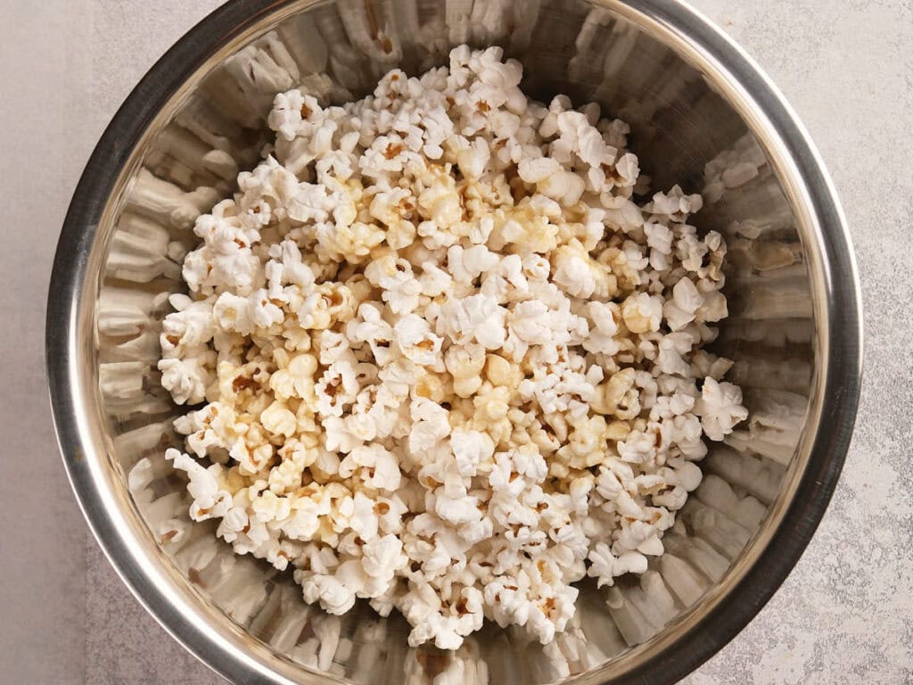 A metal bowl filled with popped popcorn sits on a light-colored surface.