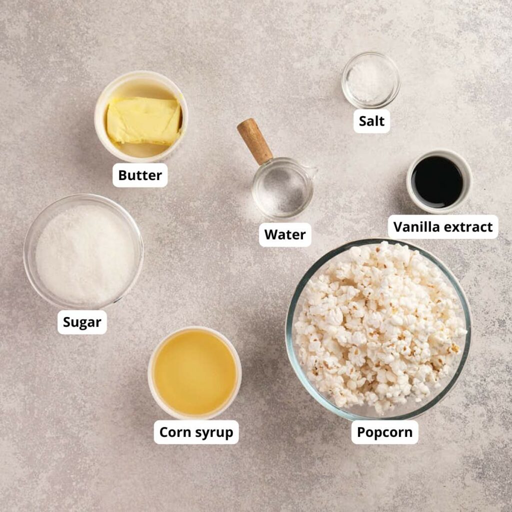 Overhead view of labeled ingredients in bowls: butter, sugar, corn syrup, water, salt, vanilla extract, and a bowl of popcorn.