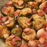 Close-up of roasted Brussels sprouts topped with crispy bacon pieces on a plate.