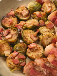 Close-up of roasted Brussels sprouts topped with crispy bacon pieces on a plate.