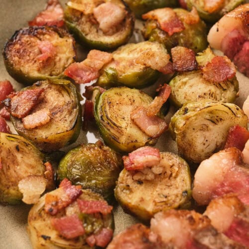 Close-up of roasted Brussels sprouts topped with crispy bacon pieces on a plate.