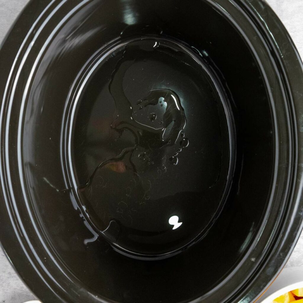 A close-up of an empty black slow cooker with a small amount of oil spread on the bottom.