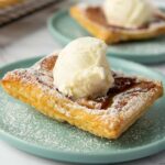 A square piece of apple puff pastry topped with a scoop of vanilla ice cream and dusted with powdered sugar.