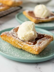 A square piece of apple puff pastry topped with a scoop of vanilla ice cream and dusted with powdered sugar.
