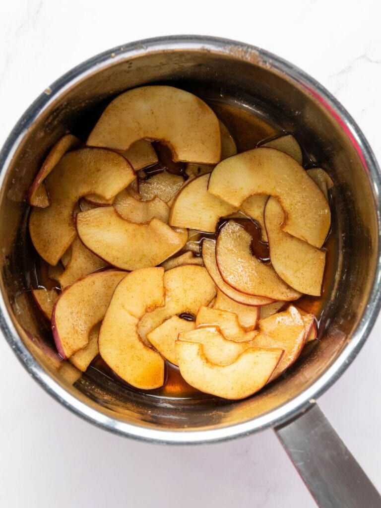 Sliced apples with cinnamon and sauce in a saucepan seen from above.