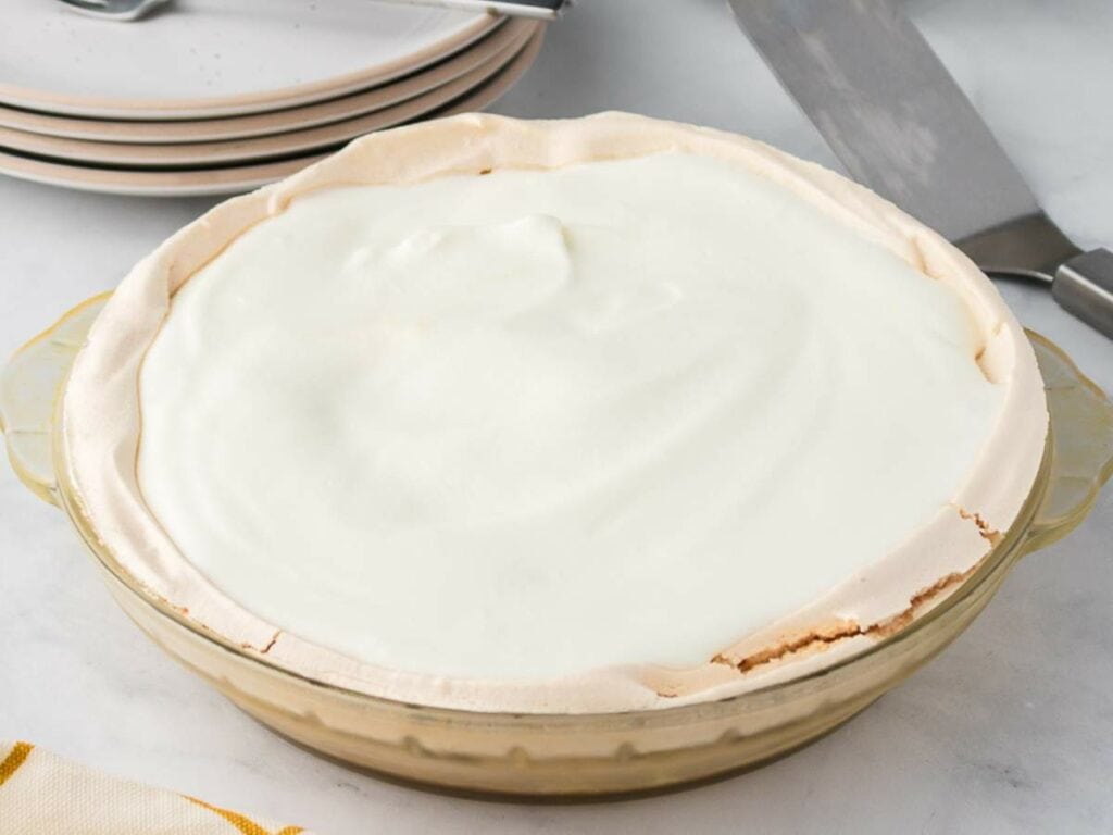A pie dish filled with a dessert topped with a smooth, white meringue layer, placed on a marble surface.