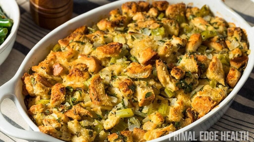 A baked casserole dish filled with golden-brown bread stuffing, mixed with chopped celery, onions, and herbs.