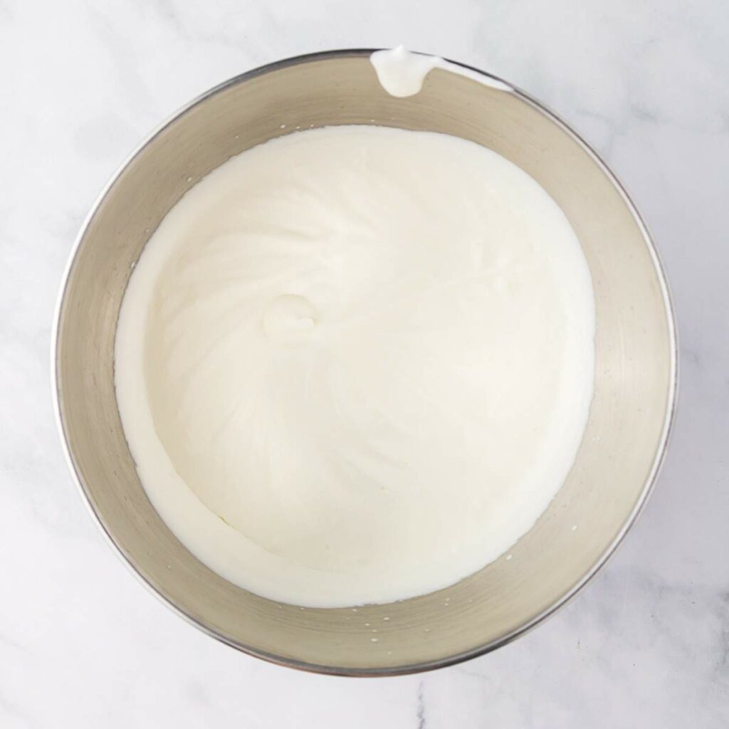 A stainless steel bowl filled with whipped cream on a white marble surface.