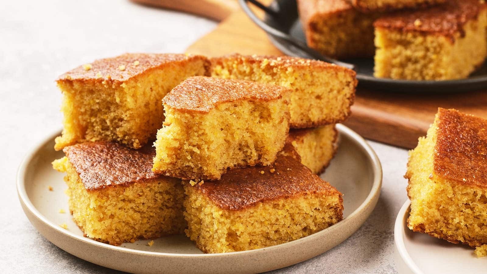 A plate with several slices of golden brown cornbread, with more pieces visible in the background on another serving dish.
