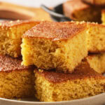 A plate with several slices of golden-brown cornbread stacked on top of each other.