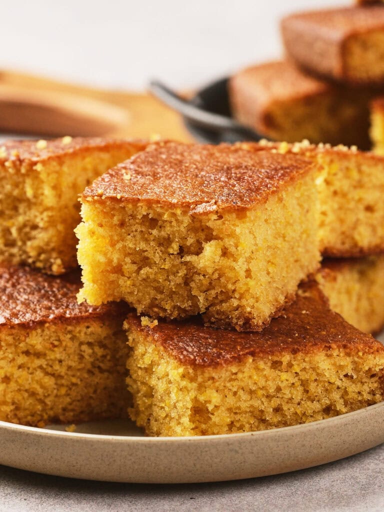 A plate with several slices of golden-brown cornbread stacked on top of each other.