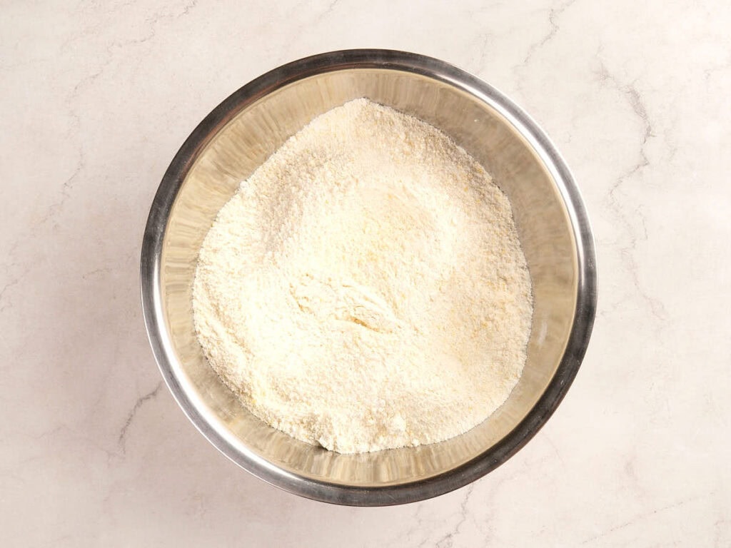 A large metal mixing bowl containing a mound of dry white flour on a light-colored countertop.