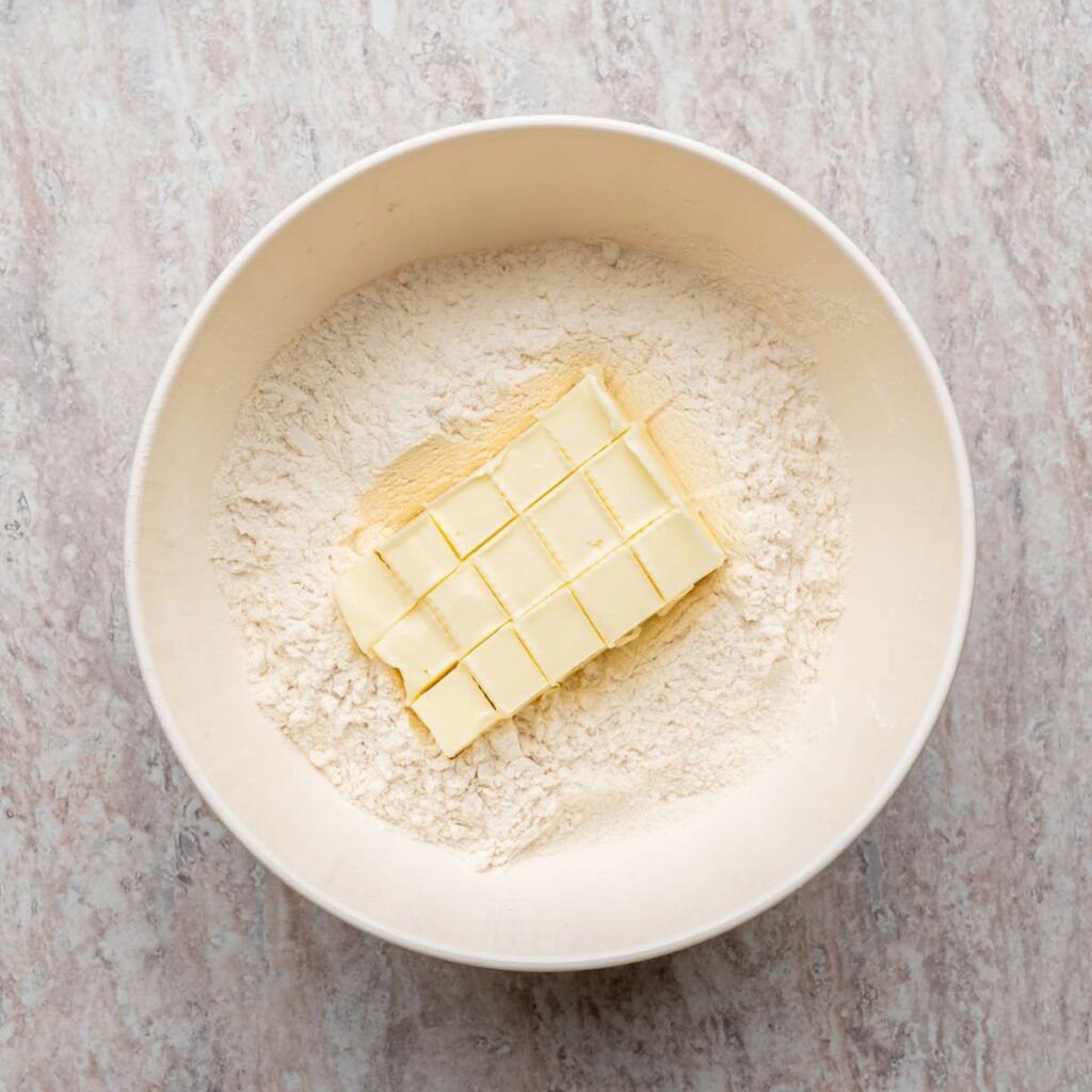 A mixing bowl containing flour and cubed butter on a light-colored countertop.