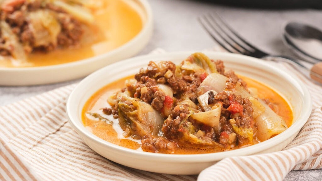 A plate of a lasagna dish, served with a striped napkin and utensils in the background.