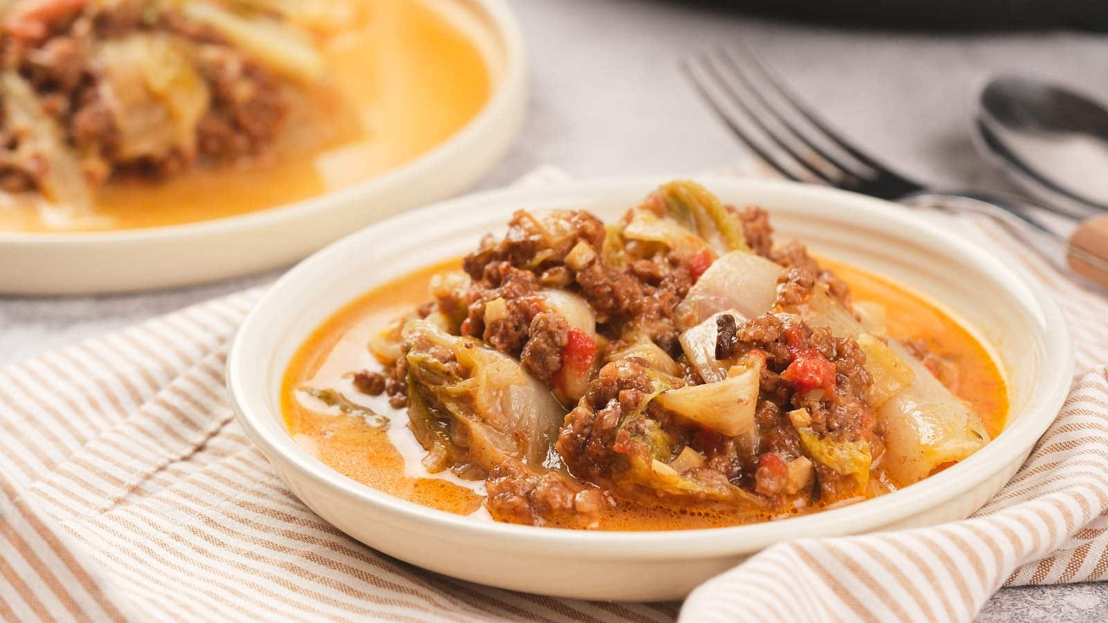 A plate of a lasagna dish, served with a striped napkin and utensils in the background.