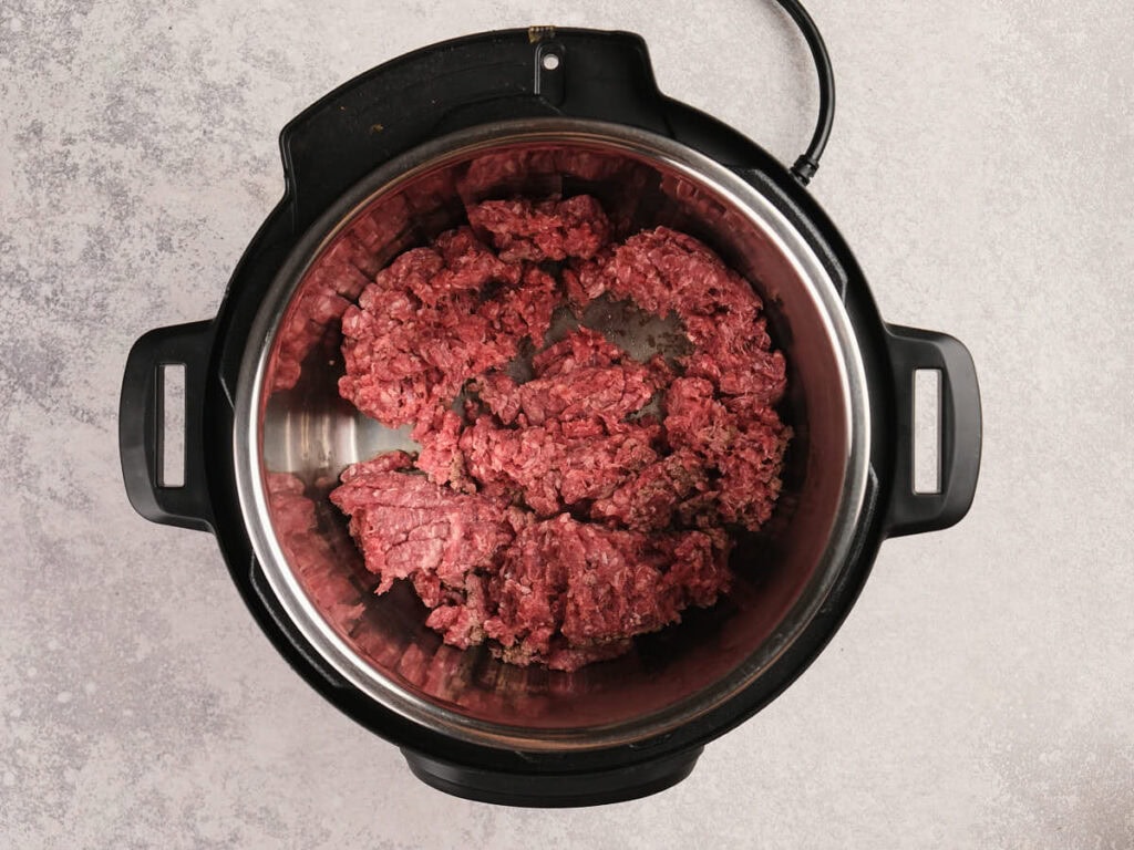 Ground beef placed in the bottom of an electric pressure cooker, viewed from above on a light countertop.