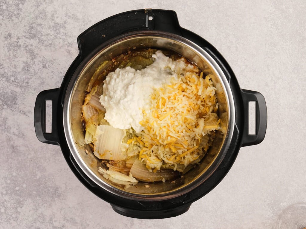 An instant pot containing cooked cabbage, onions, shredded cheese, and a dollop of cottage cheese.