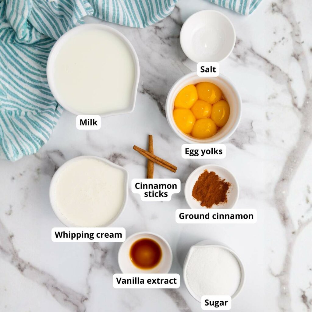 Various labeled ingredients for an eggnog recipe are arranged on a marble surface.