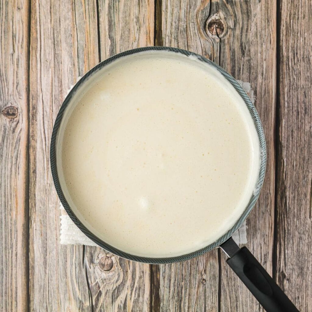 A saucepan filled with a creamy white mixture sits on a wooden surface.