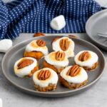 A gray plate with seven sweet potatoes topped with toasted marshmallows and pecan halves.