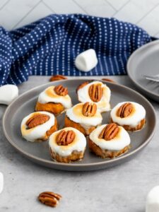 A gray plate with seven sweet potatoes topped with toasted marshmallows and pecan halves.
