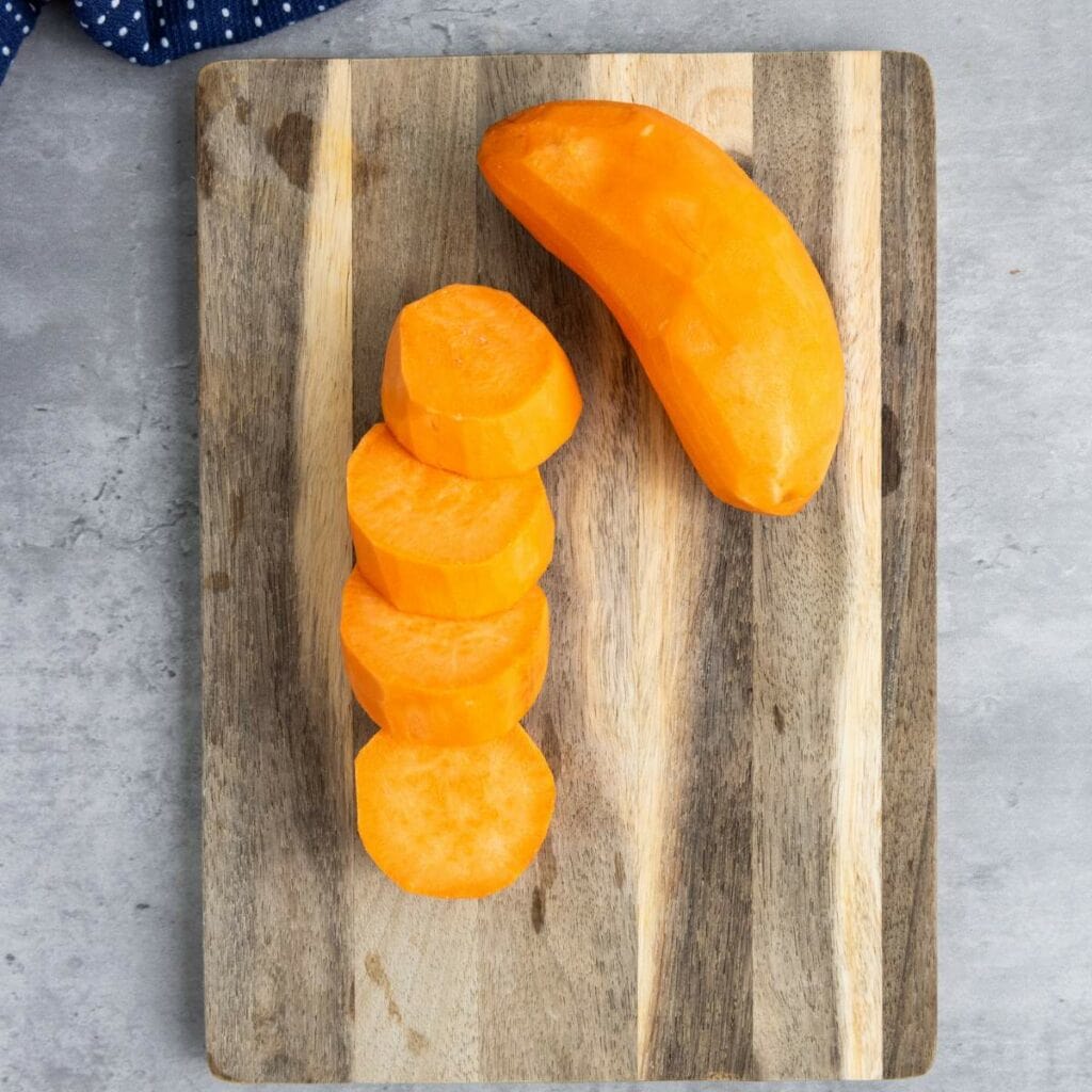 A partially sliced and peeled sweet potato on a wooden cutting board with several round slices next to the unsliced portion.