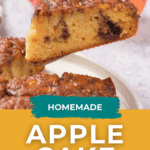 A slice of apple cake with cinnamon glaze being served, with whole apples and more cake in the background.