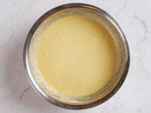 A stainless steel bowl filled with smooth, yellow cake batter sits on a light-colored countertop.