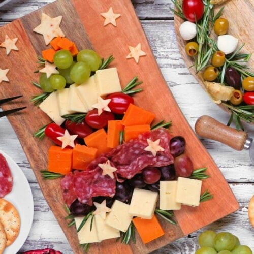 A christmas charcuterie board with assorted cheeses, grapes, salami, cherry tomatoes, and herbs.