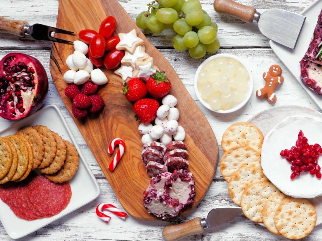 Cheeses, cherry tomatoes, strawberries, raspberries, candies, grapes, crackers, sliced meats, a pomegranate half, and a gingerbread cookie.