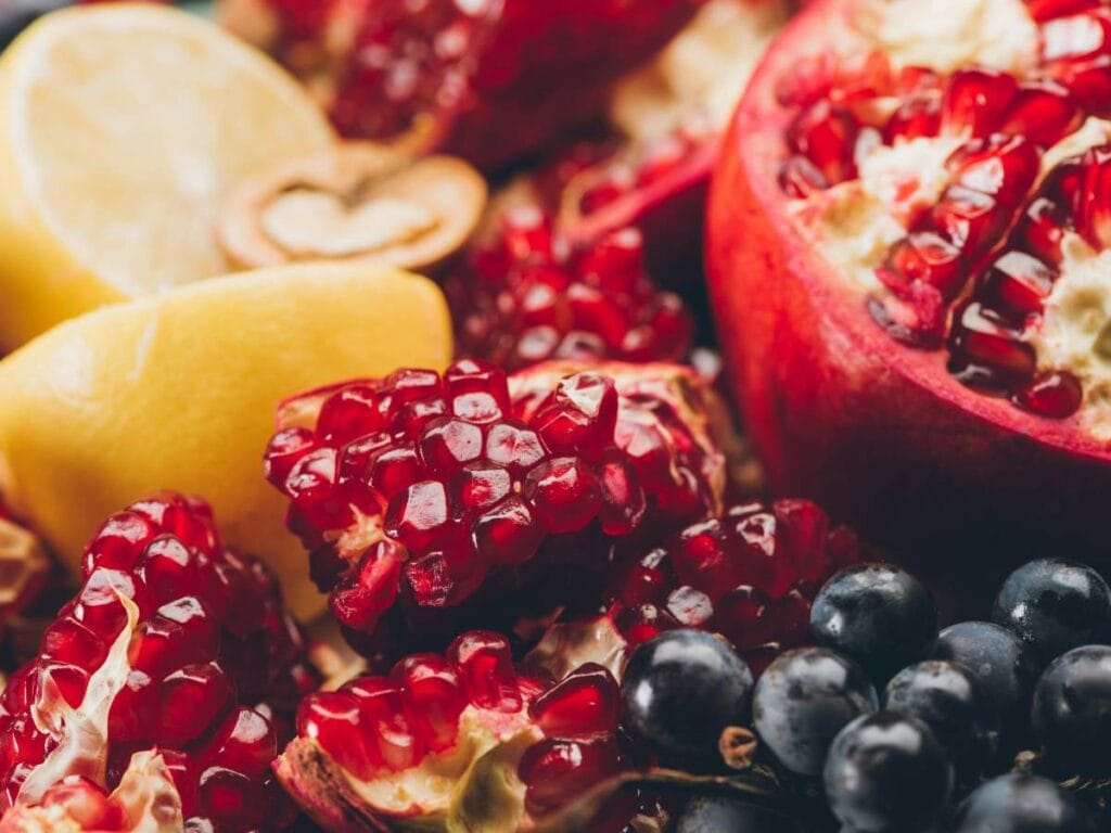 Close-up of pomegranate seeds, lemon wedges, and black grapes arranged together.