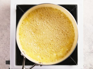 A metal pan filled with bubbling yellow liquid sits on a white stovetop burner.