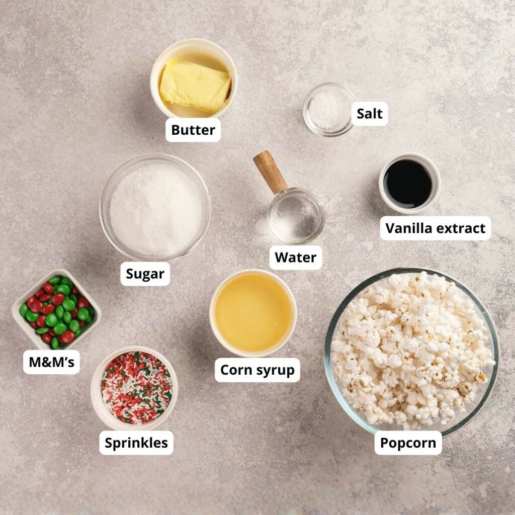 Ingredients for popcorn treats displayed on a countertop: butter, sugar, salt, water, vanilla extract, corn syrup, popcorn, sprinkles, and M&M’s.