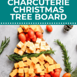 A wooden board with cheese cubes and grape tomatoes arranged in a Christmas tree shape, garnished with rosemary sprigs.