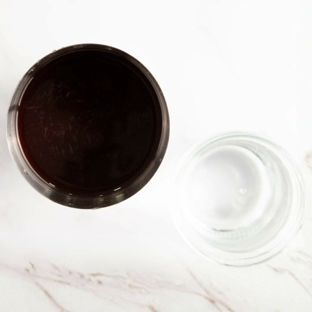 Top view of a glass filled with a dark liquid next to an empty clear glass on a white marble surface.