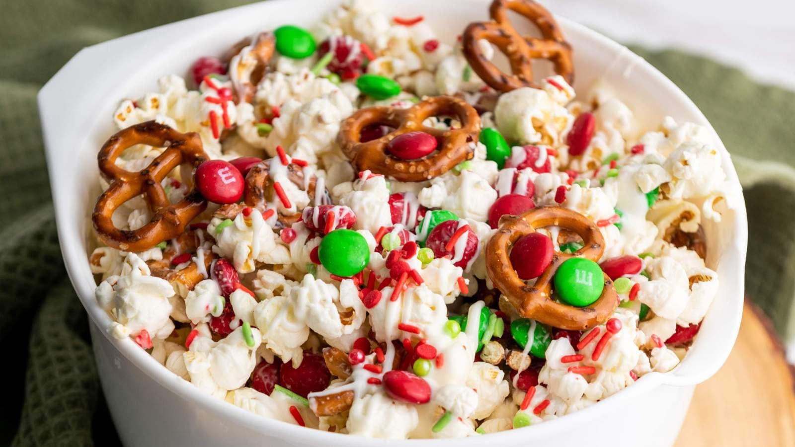 A white bowl filled with festive holiday popcorn, all drizzled with white chocolate.