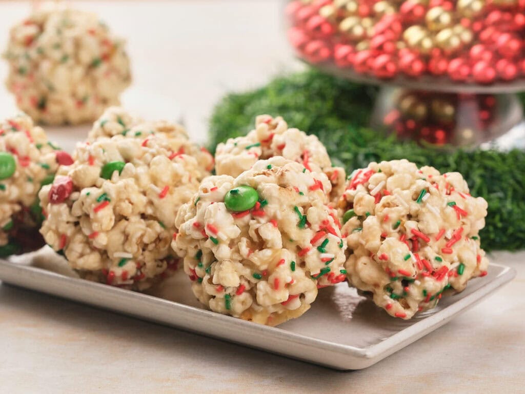 Four popcorn balls with red and green sprinkles and candy pieces are arranged on a rectangular plate.