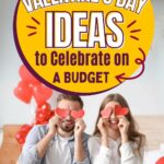 A smiling couple sits on a bed holding paper heart shapes over their eyes, surrounded by red balloons.