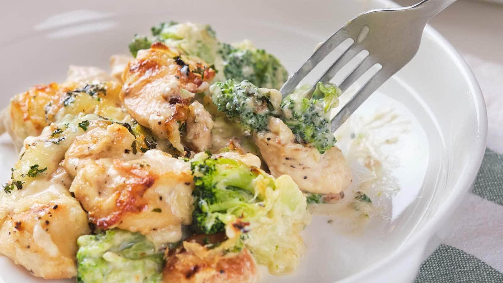 A wooden spoon scooping chicken broccoli alfredo casserole out of a serving dish.