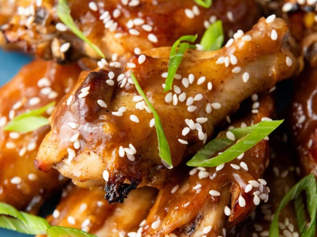 Close-up of glazed chicken wings garnished with white sesame seeds and sliced green onions.